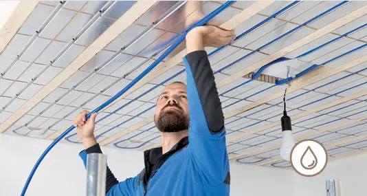 Heating engineer installing blue pipework in a water-based ceiling heating and cooling system